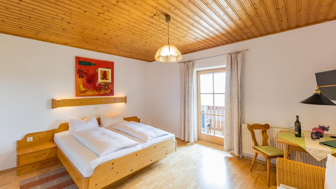 Ein gemütliches Schlafzimmer mit Holzdecke und zwei getrennten Betten. Es gibt einen Schreibtisch und einen Balkon mit Blick nach draußen.