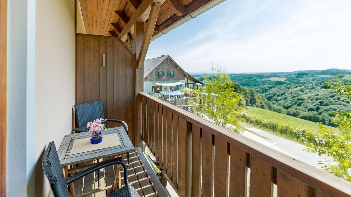 Ein schöner Balkon mit zwei Stühlen und einem Tisch. Im Hintergrund sieht man eine grüne Landschaft und einen blauen Himmel.