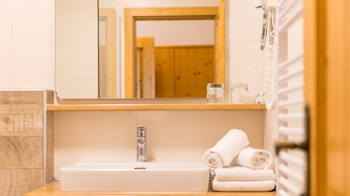 Ein modernes Badezimmer mit einem Waschbecken und frischen Handtüchern. Im Hintergrund sind Holzdetails und ein Spiegel sichtbar.
