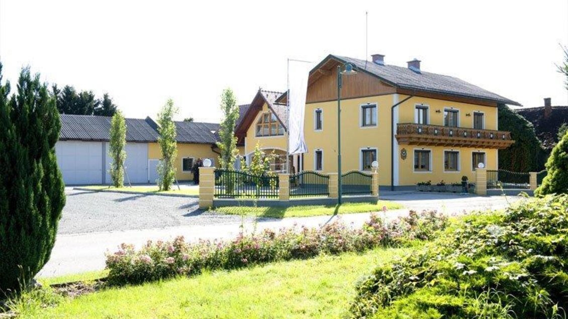 Ein elegantes, gelbes Haus mit einem Holzdach und einer gepflegten Umgebung. Es gibt eine Auffahrt und Bäume, die die Einfahrt säumen. | © Weingut Reinisch