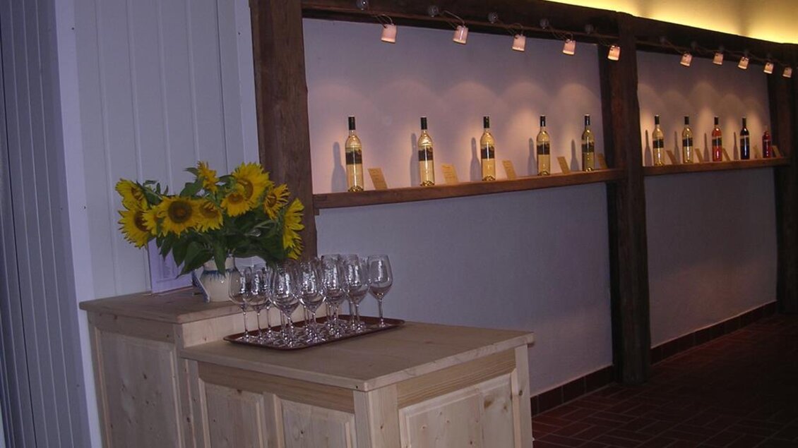 Ein gemütlicher, elegant gestalteter Raum mit einer Holztheke und Gläsern. Im Hintergrund stehen Flaschen auf Regalen und frische Sonnenblumen schmücken die Theke. | © Weingut Rupp