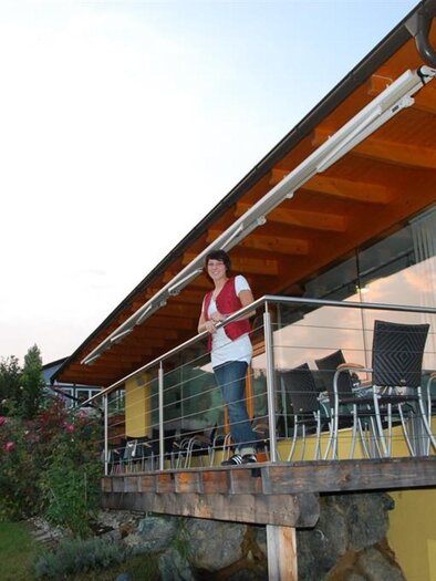 A modern house with a terrace and garden. One person is standing on the terrace and looking outside. | © Weingut &  Buschenschank Stefanie Sauer