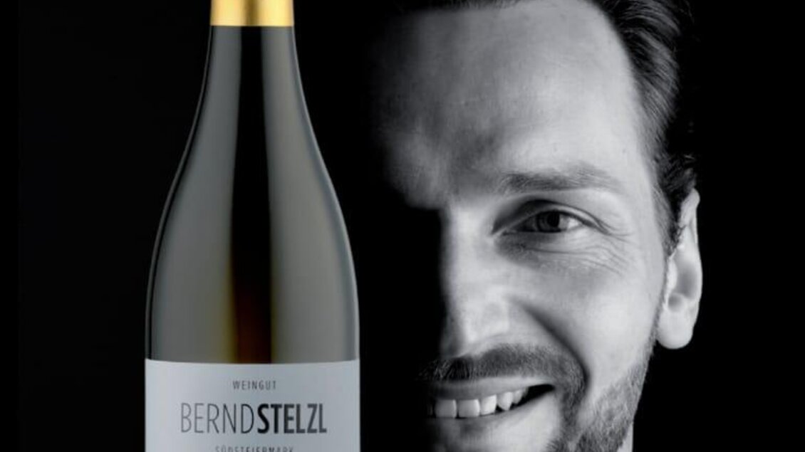 Ein stilvolles Portrait eines Mannes, der neben einer Flasche Wein steht. Der Hintergrund ist schwarz, um die Präsentation hervorzuheben. | © Weingut Bernd Stelzl