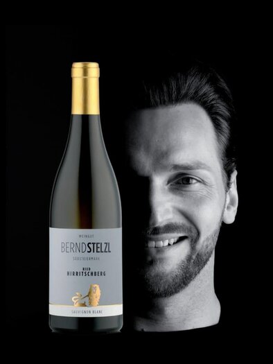 A stylish portrait of a man standing next to a bottle of wine. The background is black to highlight the presentation. | © Weingut Bernd Stelzl