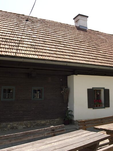 A traditional country house with a red tiled roof and wooden facade. In front of the house is a wooden bench. | © Weingut Wölfl / Familie Schilcher