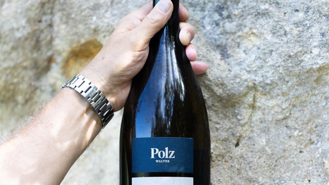 Eine Hand hält eine Flasche weißen Wein mit dem Etikett "Polz stone white". Im Hintergrund ist eine natürliche Steinoberfläche sichtbar. | © Weingut Walter Polz