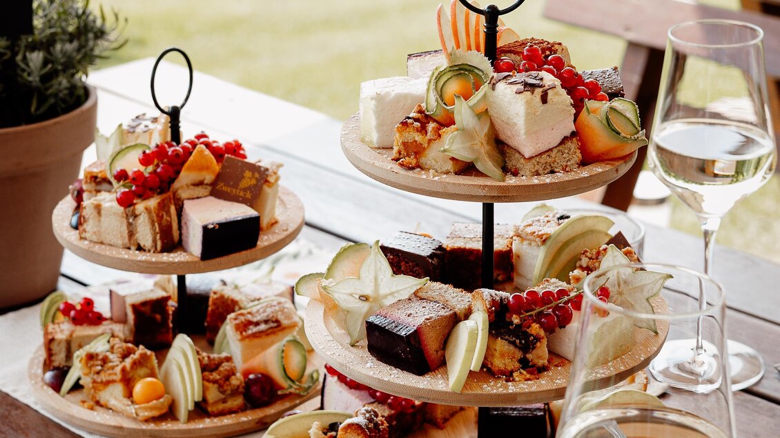 Ein schön dekorierter Tisch mit drei Etagen von köstlichen Snacks und Desserts. Im Hintergrund sind Weinreben zu sehen und es gibt Gläser mit Weißwein. | © Katja Koller