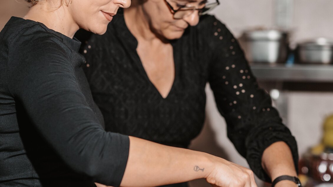 Zwei Frauen bereiten gemeinsam eine köstliche Auswahl an Speisen in einer modernen Küche vor. Sie konzentrieren sich auf das Anrichten der Gerichte mit frischen Zutaten. | © Michaela Lorber