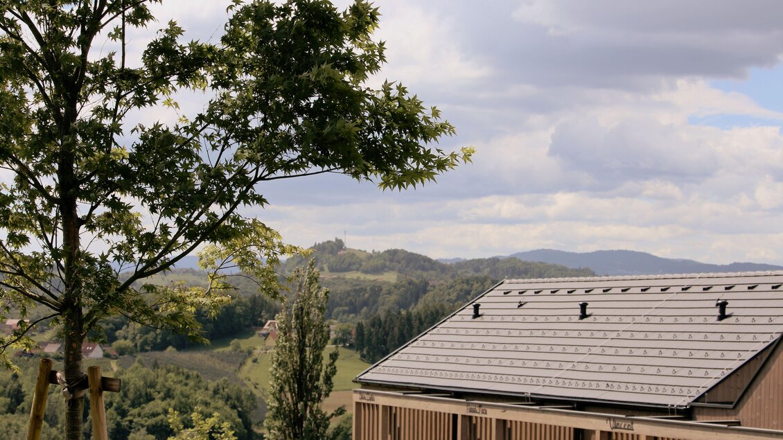 Ein modernes Gebäude mit einem Dach aus Ziegeln. Im Hintergrund erstrecken sich sanfte Hügel und ein bewölkter Himmel. | © Elena Zweytick