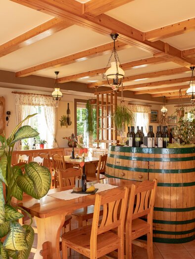 Ein gemütliches Restaurant mit Holzmöbeln und einer großen Weinfass als Tisch. Pflanzen und Fenster sorgen für eine einladende Atmosphäre. | © GlaMUR-Genuss am Fluss, Ulrike Korntheuer