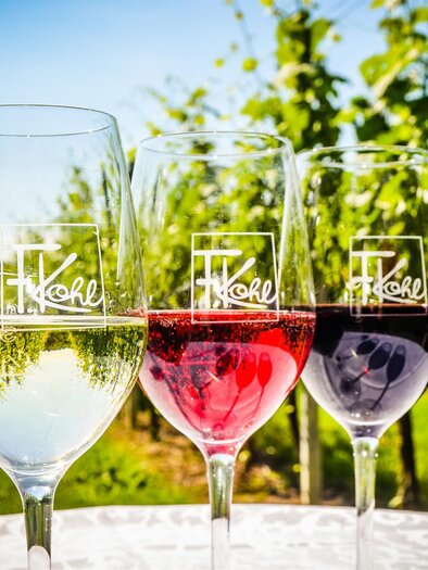 Drei Gläser Wein stehen vor einem Weinberg. Das erste Glas enthält weißen Wein, das zweite roséfarbene und das dritte roten Wein. | © Arthur Michalek