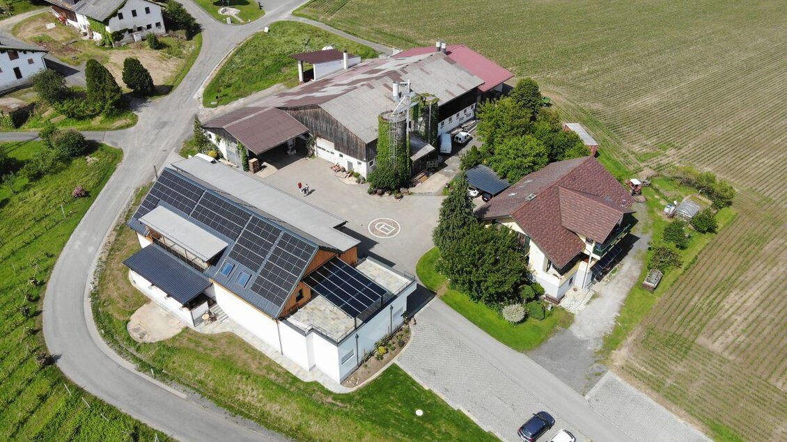 Eine Airview von einem Bauernhof mit Gebäuden und einem großen Solarpanel. Umgeben von Feldern und einer ruhigen Landstraße. | © Weinhof Tropper