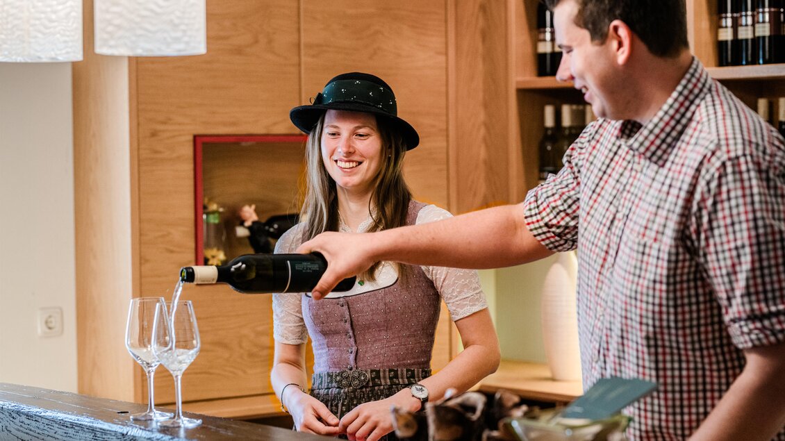Eine Person schenkt Wein in zwei Gläser in einer Weinbar ein. Die warmen Holzfarben schaffen eine gemütliche Atmosphäre. | © Florfotografie