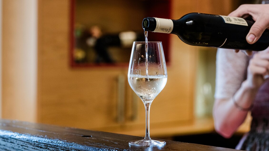 Ein Glas Wein wird gerade aus einer Flasche eingeschenkt. Der Hintergrund zeigt eine moderne, helle Küche. | © Florfotografie