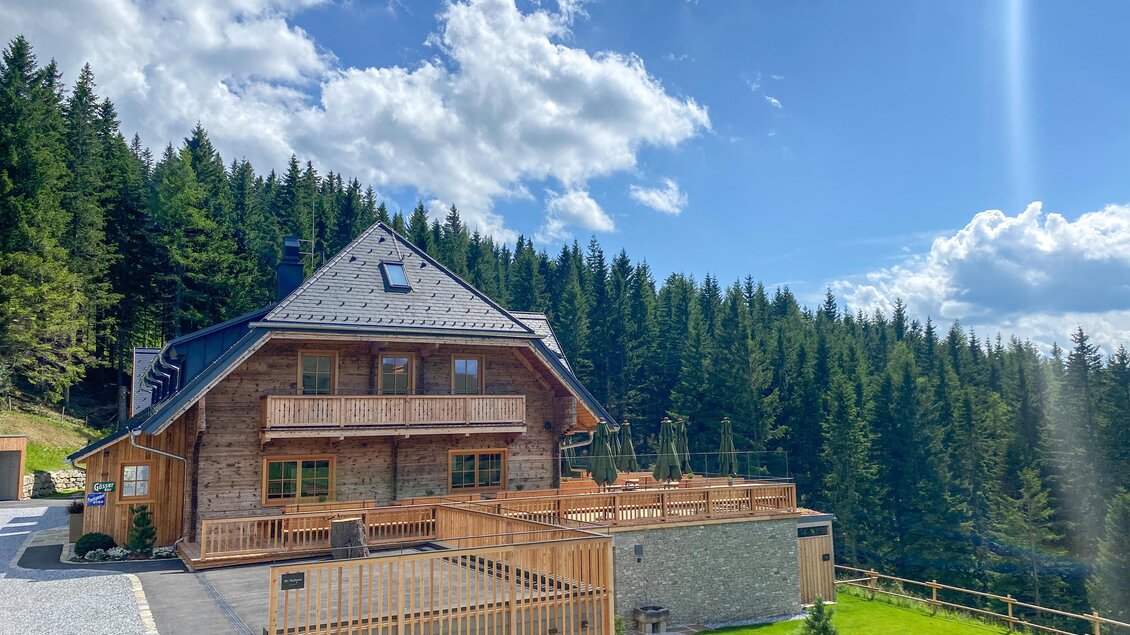 Ein modernes Holzhaus umgeben von einem grünen Wald. Der Himmel ist blau mit einigen Wolken. | © Oststeiermark Tourismus