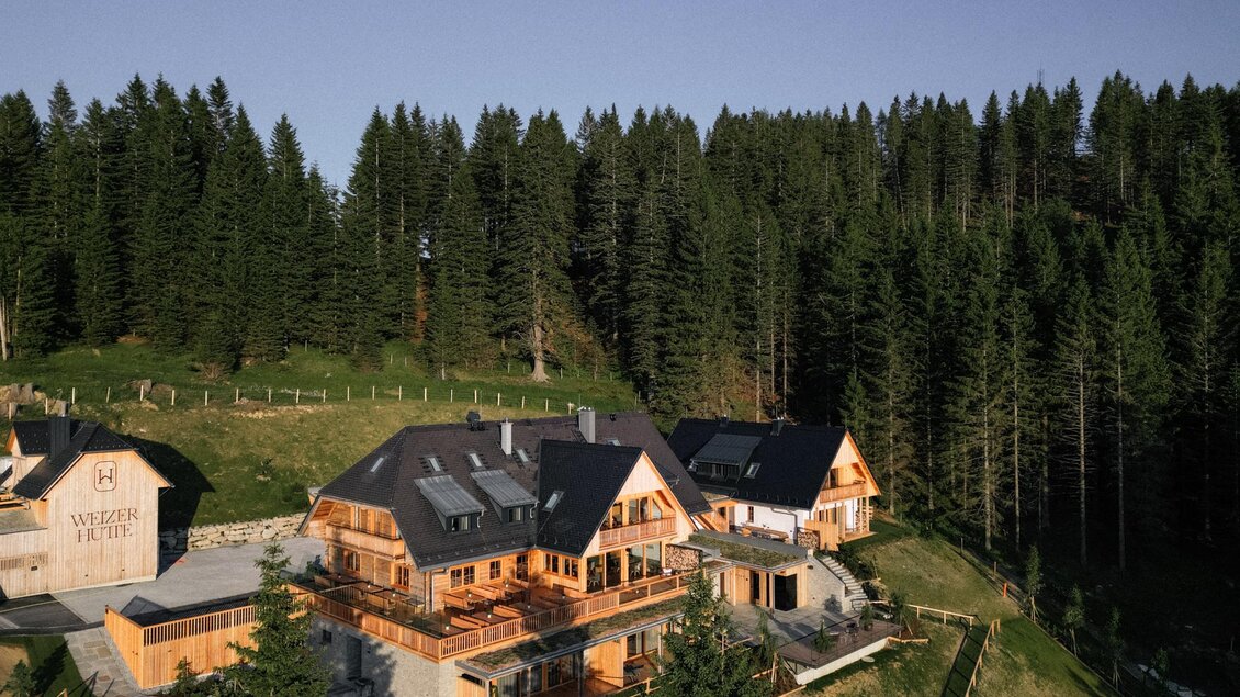 Ein modernes Holzhaus inmitten eines bewaldeten Gebiets. Die Umgebung ist grün und lädt zur Erholung in der Natur ein. | © Weizerhütte