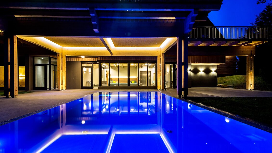 Ein modernes Haus mit einem glitzernden blauen Pool im Vordergrund. Die Architektur ist elegant und die Beleuchtung schafft eine entspannte Atmosphäre in der Nacht. | © Der Klugbauer