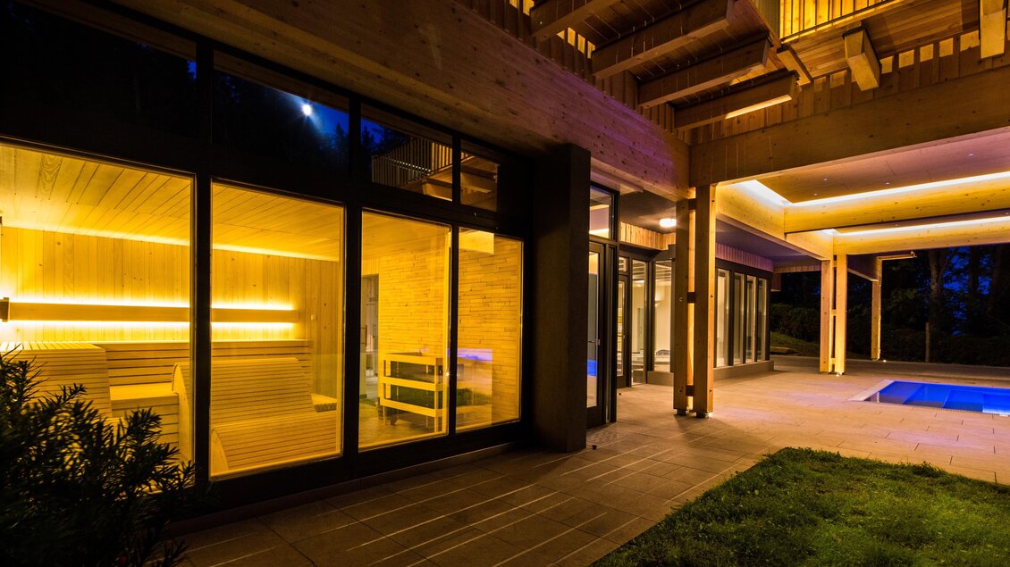 Ein moderner Außenbereich mit beleuchteter Sauna und Pool. Die Architektur ist elegant und einladend, umgeben von einem gepflegten Garten. | © Der Klugbauer