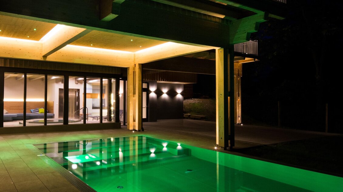 Ein modernes Haus mit einem beleuchteten Pool. Die grüne Wasseroberfläche reflektiert das Licht der Umgebung. | © Der Klugbauer