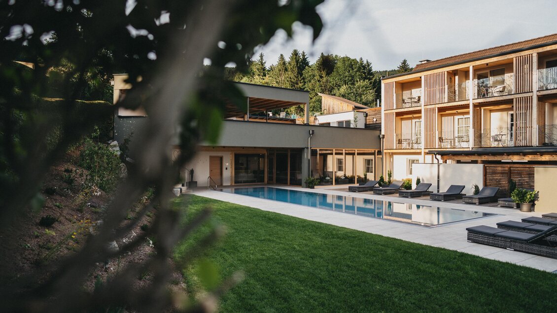 Ein modernes Hotel mit einem eleganten Pool und gemütlichen Liegen im Außenbereich. Die grüne Rasenfläche und die umgebende Natur schaffen eine entspannte Atmosphäre. | © Heldentheater