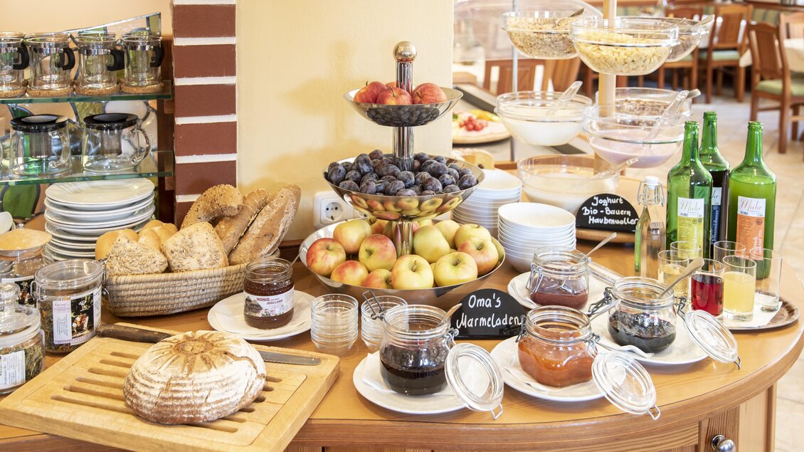 Ein reichhaltiges Frühstücksbuffet mit frischem Obst, Müsli und verschiedenen Marmeladen. Es gibt auch Brot und Getränke auf dem Tisch. | © Gasthof Orthofer