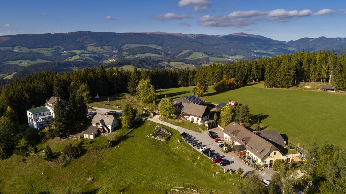 Eine malerische Landschaft mit sanften Hügeln und Wäldern. Mehrere Gebäude liegen zwischen grünen Wiesen in der Ferne. | © Gasthof Orthofer
