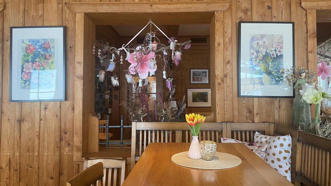 Ein gemütlicher Essbereich mit Holzwänden und einem Tisch in der Mitte. Auf dem Tisch steht eine Vase mit bunten Tulpen und Dekorationselemente. | © Bettina Scheck