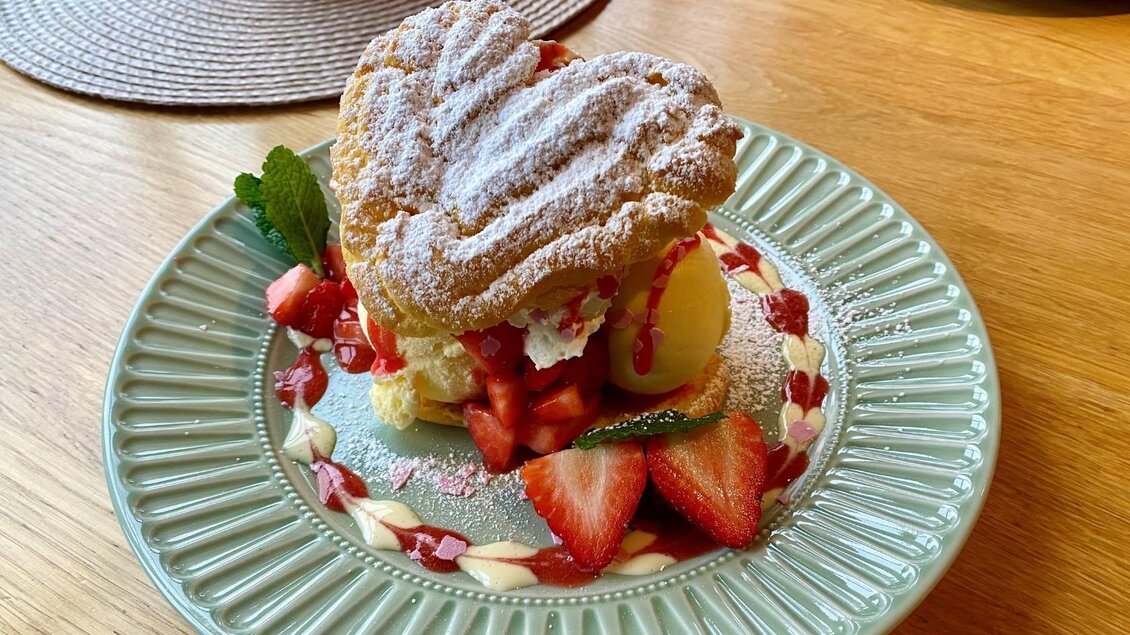 Ein herzförmiges Dessert aus Gebäck, gefüllt mit Sahne und frischen Erdbeeren. Es ist dekoriert mit Puderzucker und Minze auf einem schönen Teller. | © Bettina Scheck