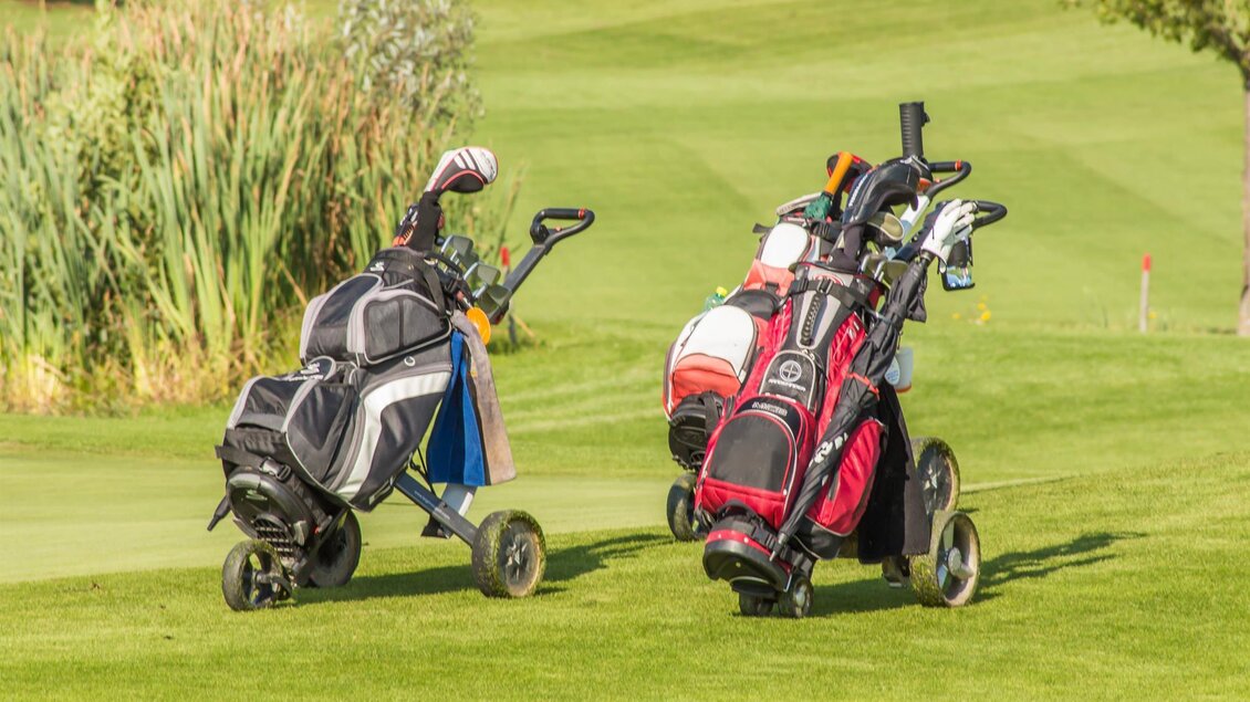 Zwei Golftaschen stehen auf einer grünen Wiese. Im Hintergrund sind hohe Gräser zu sehen. | © Ingrid Jansky