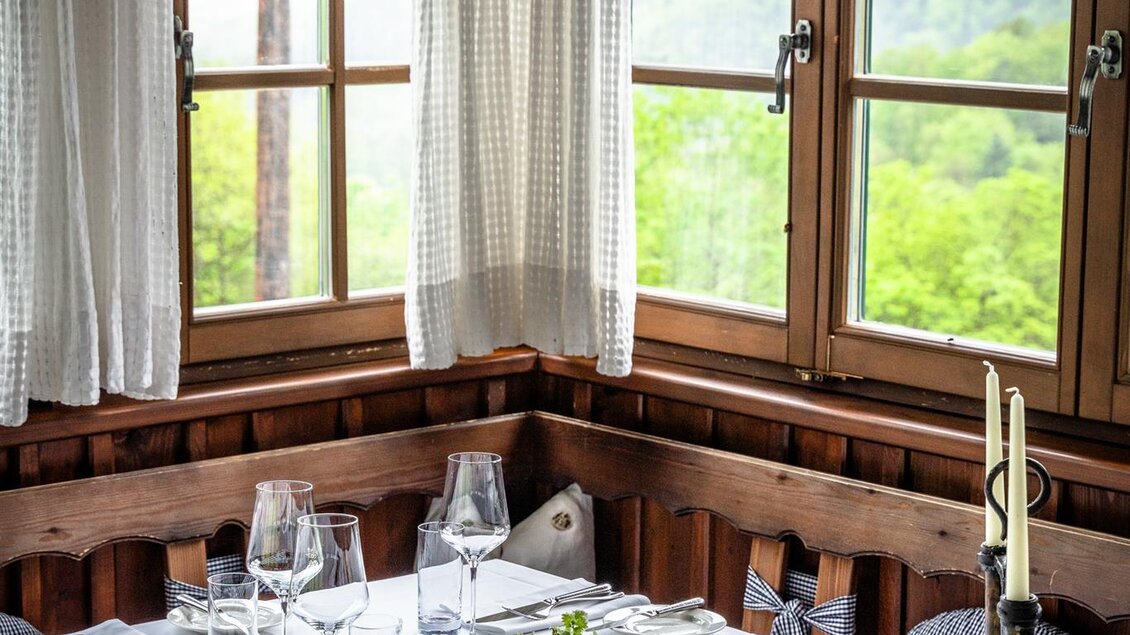 Ein einladendes Restaurant mit einem Tisch, der schön gedeckt ist. Die großen Fenster bieten einen Blick auf die grüne Landschaft. | © Stephan Friesinger
