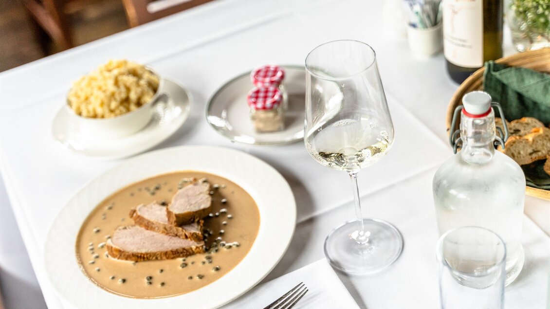Ein schön gedeckter Tisch mit einer Fleischmahlzeit in einer cremigen Sauce, serviert mit Brot. Dazu gibt es einen Salat, einen Wein und ein Dessert. | © Stephan Friesinger