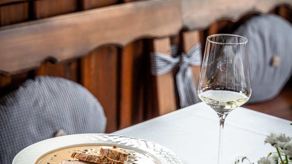 Ein schön gedeckter Tisch mit einem Teller Pasta, Brot und einem Glas Wein. Im Hintergrund sind Fenster und eine Holzverkleidung zu sehen. | © Stephan Friesinger