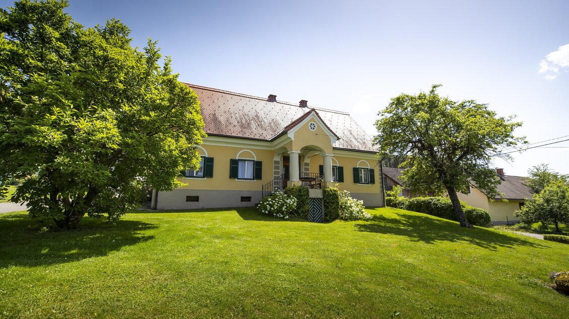Ein schönes Haus umgeben von grünem Gras und Bäumen. Der Himmel ist klar und sonnig. | © Winzerhof Strablegg