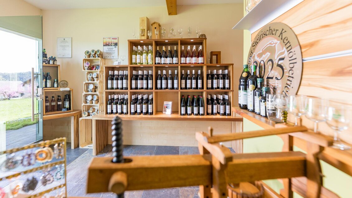Ein einladender Verkaufsraum mit Regalen voller Flaschen und Produkten. Auf einer Theke stehen verschiedene Weingläser und eine Holzpresse. | © Winzerhof Strablegg