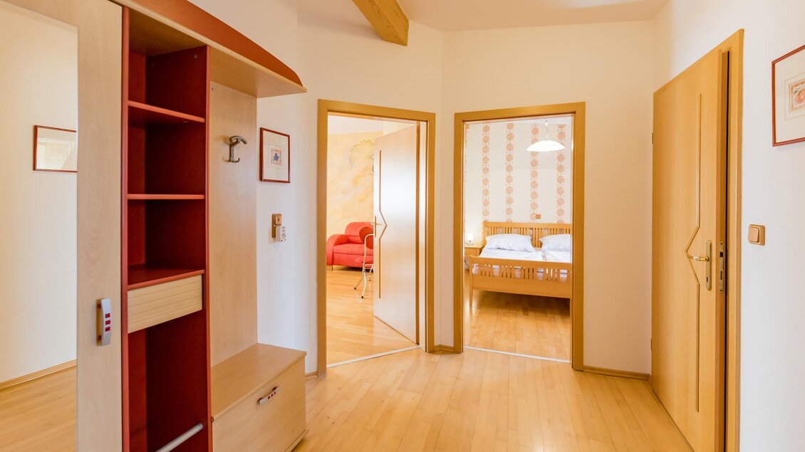Ein heller Flur mit Holzboden und modernen Möbeln. Im Hintergrund sieht man ein Schlafzimmer mit einem Doppelbett. | © Winzerhof Strablegg