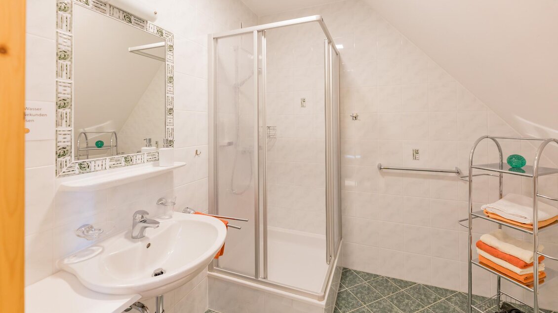 Ein modernes Badezimmer mit einer Dusche und einem Waschbecken. Die Wände sind hell gefliest und es gibt ein Regal mit Handtüchern. | © Winzerhof Strablegg