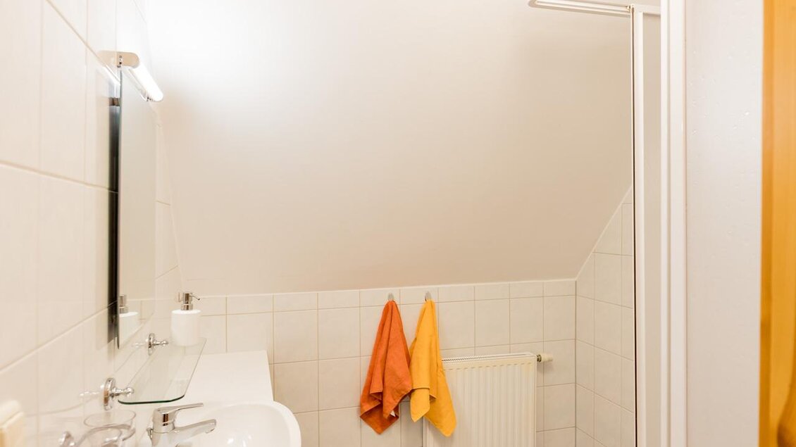 Ein helles Badezimmer mit Dusche und Badewanne. Zwei Handtücher in Orange und Gelb hängen an der Wand. | © Winzerhof Strablegg