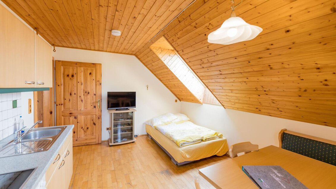 Ein gemütliches Zimmer mit Holzdecke und Holzmöbeln. Es gibt eine kleine Küche, ein Bett und einen Tisch mit Stühlen. | © Winzerhof Strablegg
