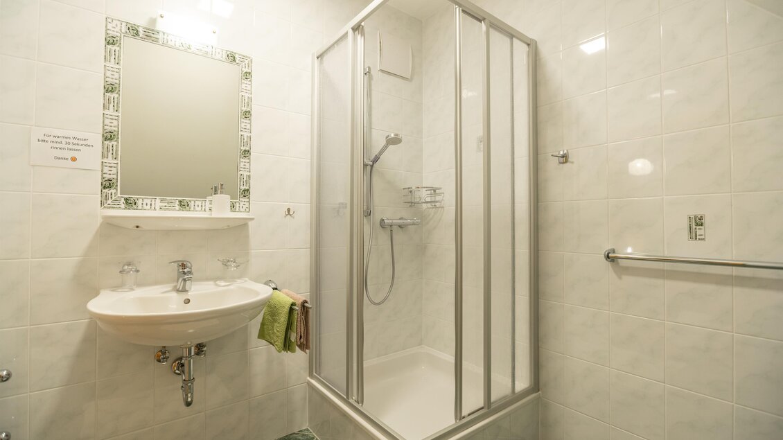 Ein modernes Badezimmer mit einer Duschkabine und einem Waschbecken. Die Wände sind hell gefliest und ein Spiegel hängt über dem Waschbecken. | © Winzerhof Strablegg