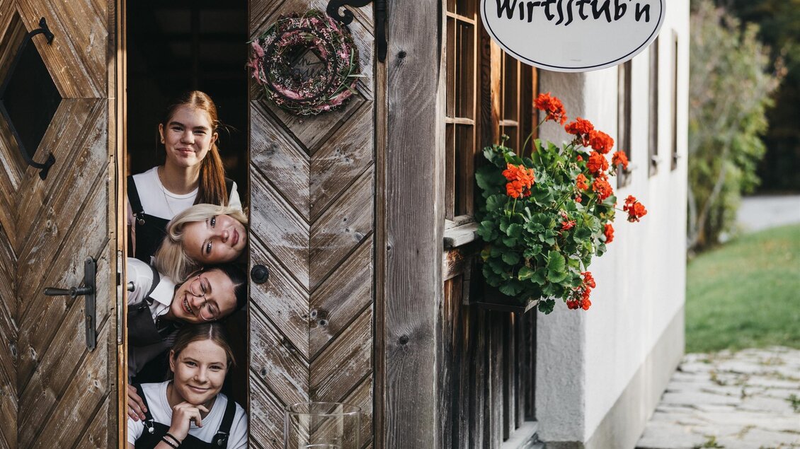 Einladendes Wirtshaus mit Holzfassade. Vier Personen stehen lächelnd in der Tür und zeigen eine freundliche Atmosphäre. | © Heldentheater
