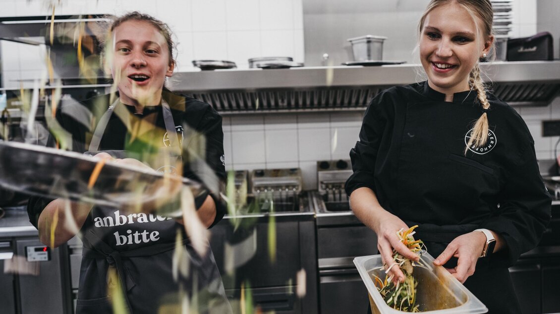 Zwei Köchinnen lächeln in einer modernen Küche. Sie bereiten frische Zutaten vor und arbeiten mit großer Freude. | © Heldentheater