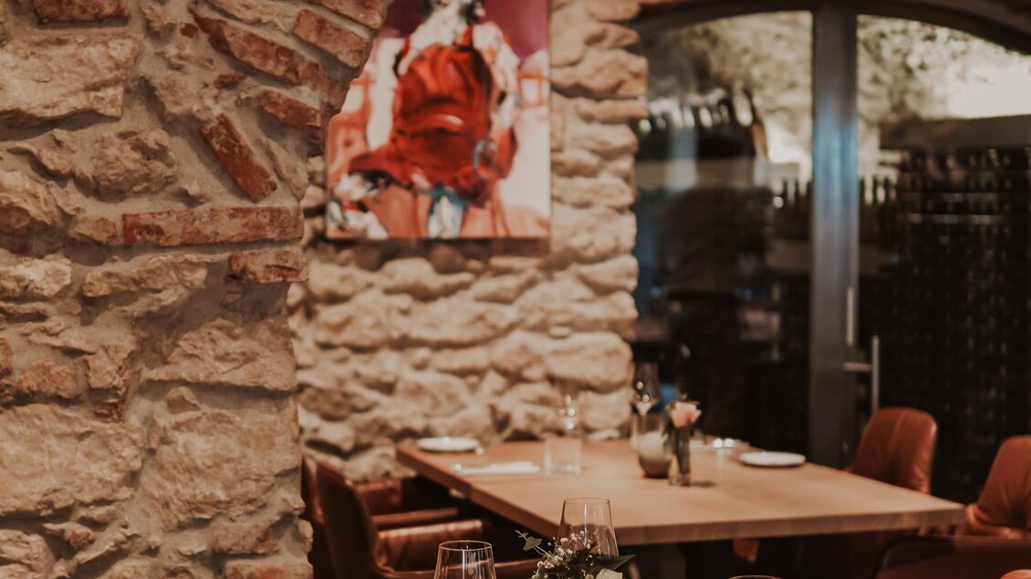 Ein gemütliches Restaurant mit Steinmauern und einer eleganten Tischdekoration. An der Wand hängt ein auffälliges Kunstwerk. | © Yvonne Bernhard