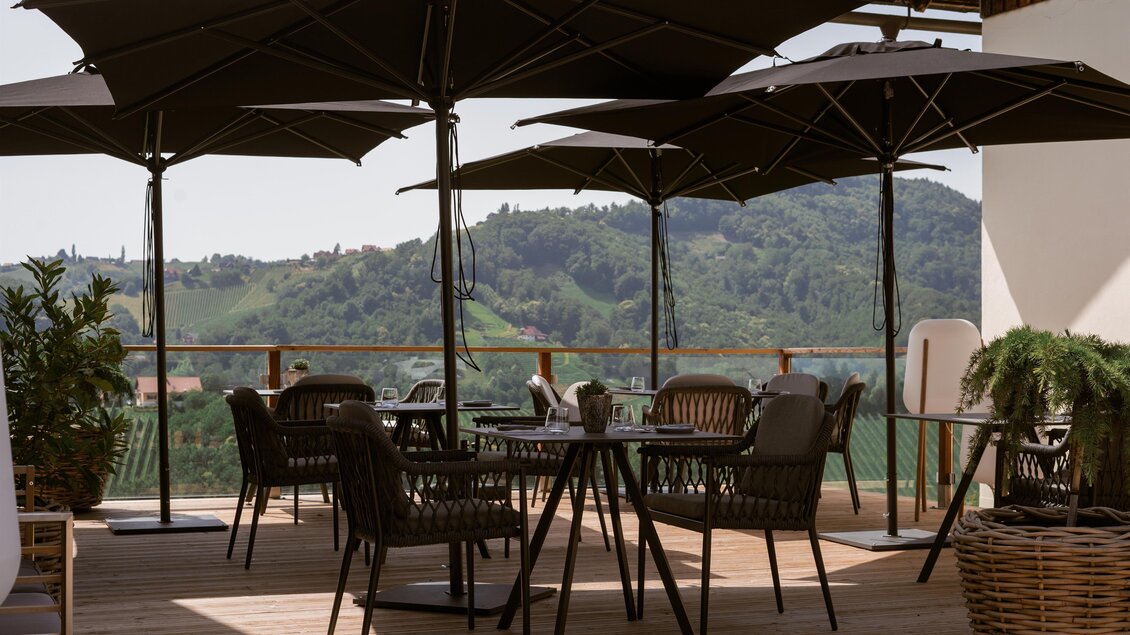 Eine entspannte Terrasse mit schwarzen Sonnenschirmen und modernen Möbeln. Der Blick geht über sanfte grüne Hügel. | © Das Weinkitz