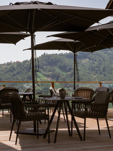 Eine entspannte Terrasse mit schwarzen Sonnenschirmen und modernen Möbeln. Der Blick geht über sanfte grüne Hügel. | © Das Weinkitz