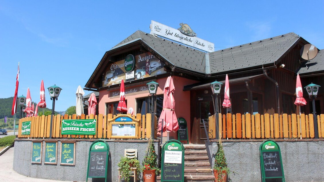 Ein gemütliches Restaurant mit einer einladenden Fassade. Vor dem Eingang stehen rot-weiße Sonnenschirme und Schilder mit Speiseangeboten. | © TVB Ausseerland - Salzkammergut_Viola Lechner