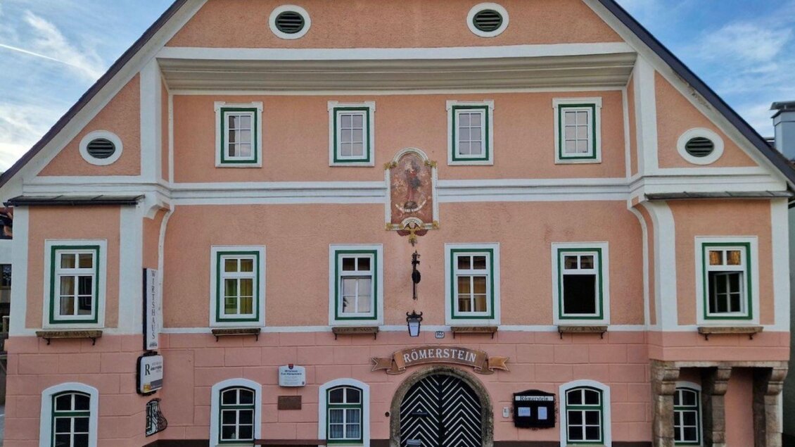 <p>Ein einladender Gasthof mit historischer Fassade, auf welcher der Name "Römerstein" steht, und einer markanten zweifarbigen Tür. Die rosane Fassade ist freundlich und hat grüne Fensterrahmen.</p> | © Gerhard Fallent