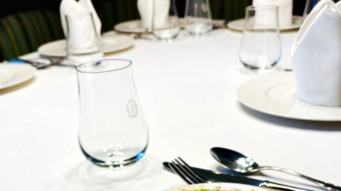 Ein elegant gedeckter Tisch mit weißer Tischdecke, Besteck und Gläsern. Im Vordergrund befindet sich ein Teller mit einem hübschen Design. | © Wirtshaus zum Römerstein