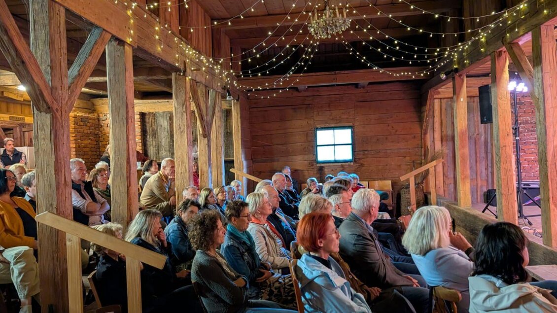 Eine Veranstaltung im oberen Bereich des Woferlstalls mit vielen Zuschauern, welche zwischen der traditionellen Holzkonstruktion Platz genommen haben. Die ehemalige Scheune wurde mit leuchtenden Lichterketten verziert. | © Eike Forum