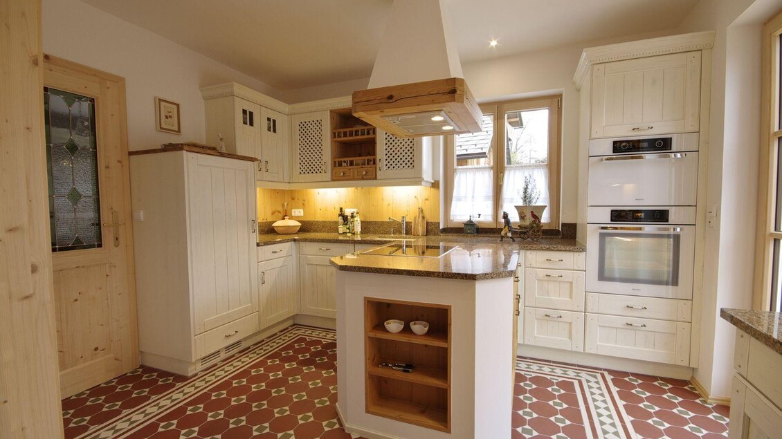 Moderne Küche mit einer eleganten Kücheninsel aus Marmor und Holzboden. Helle Farben und stilvolle Möbel sorgen für ein einladendes Ambiente. | © Grill und Ronacher