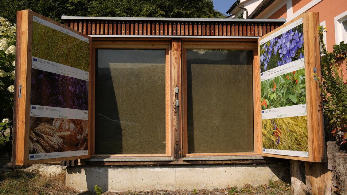 Ein Holzschrank mit Glasscheiben, der mit verschiedenen Pflanzenmotiven dekoriert ist. Der Schrank steht in einer grünen Umgebung. | © Tourismusverband Oststeiermark